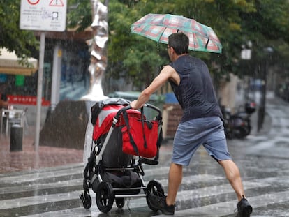 Un padre (de espaldas) empuja un carrito de bebé bajo la lluvia en Terrassa (Barcelona), en una imagen de archivo.
