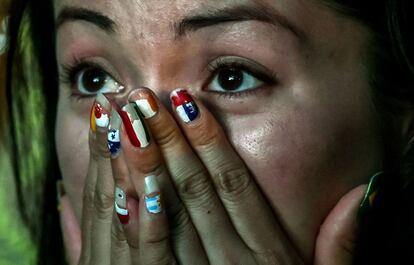 Uma mulher parece não acreditar no que vê, com as unhas pintadas das bandeiras de vários países, entre elas a do Brasil, no polegar.