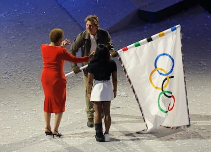 el actor norteamericano Tom Cruise entrega la bandera olímpica a la alcaldesa de Los Ángeles, Karen Bass, en presencia de Simone Biles (de espaladas).