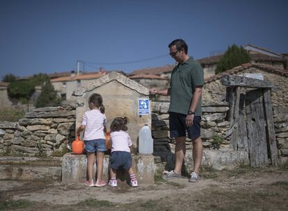 Vecino del pueblo sacando agua de la fuente junto a sus hijas.