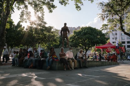 Vecinos descansan cerca de una estatua de Simón Bolívar mientras voluntarios instruyen sobre cómo votar el 21 de noviembre, en Caracas.