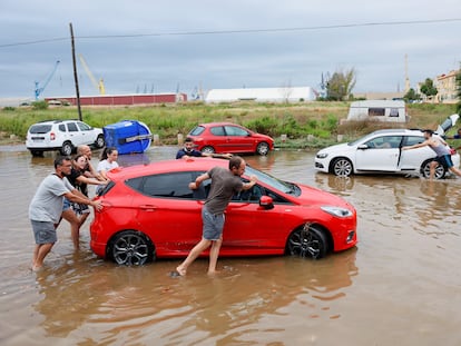 Varias personas arrastran sus coches afectados por la tromba de agua en Puerto de Sagunto.