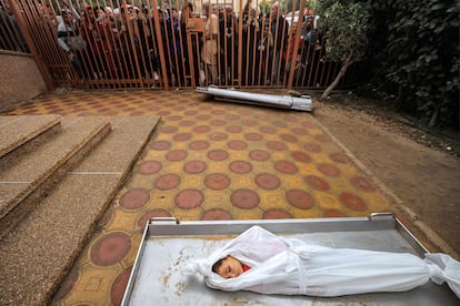 Varias personas permanecen de pie detrás de una verja frente al cuerpo de un niño, entre otros, víctima de un  bombardeo israelí, este martes antes de ser enterrado, en la morgue del hospital Nasser, en Jan Yunis. 