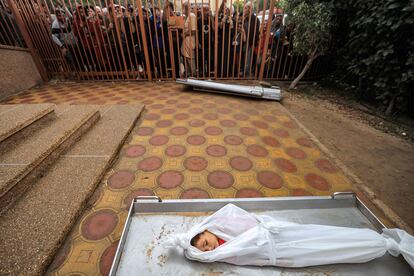 Varias personas permanecen de pie detrás de una verja frente al cuerpo de un niño, entre otros, víctima de un  bombardeo israelí, este martes antes de ser enterrado, en la morgue del hospital Nasser, en Jan Yunis. 