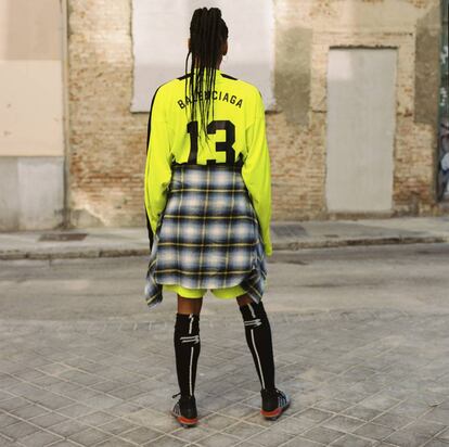 Camiseta de manga larga y shorts de fútbol en amarillo neón y negro, con calcetines altos en algodón técnico blanco y negro, todo de Balenciaga; zapatillas de fútbol de Adidas y, atada a la cintura, camisa de lana y algodón de Levi’s California.