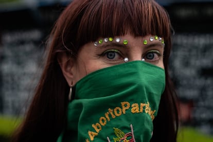 Una chica maquillada y cubierta con un pañuelo verde mira a la cámara.