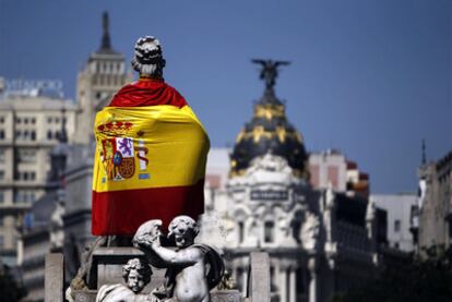 Una bandera de España rodea la estatua de la diosa Cibeles, con el edificio Metrópolis al fondo.