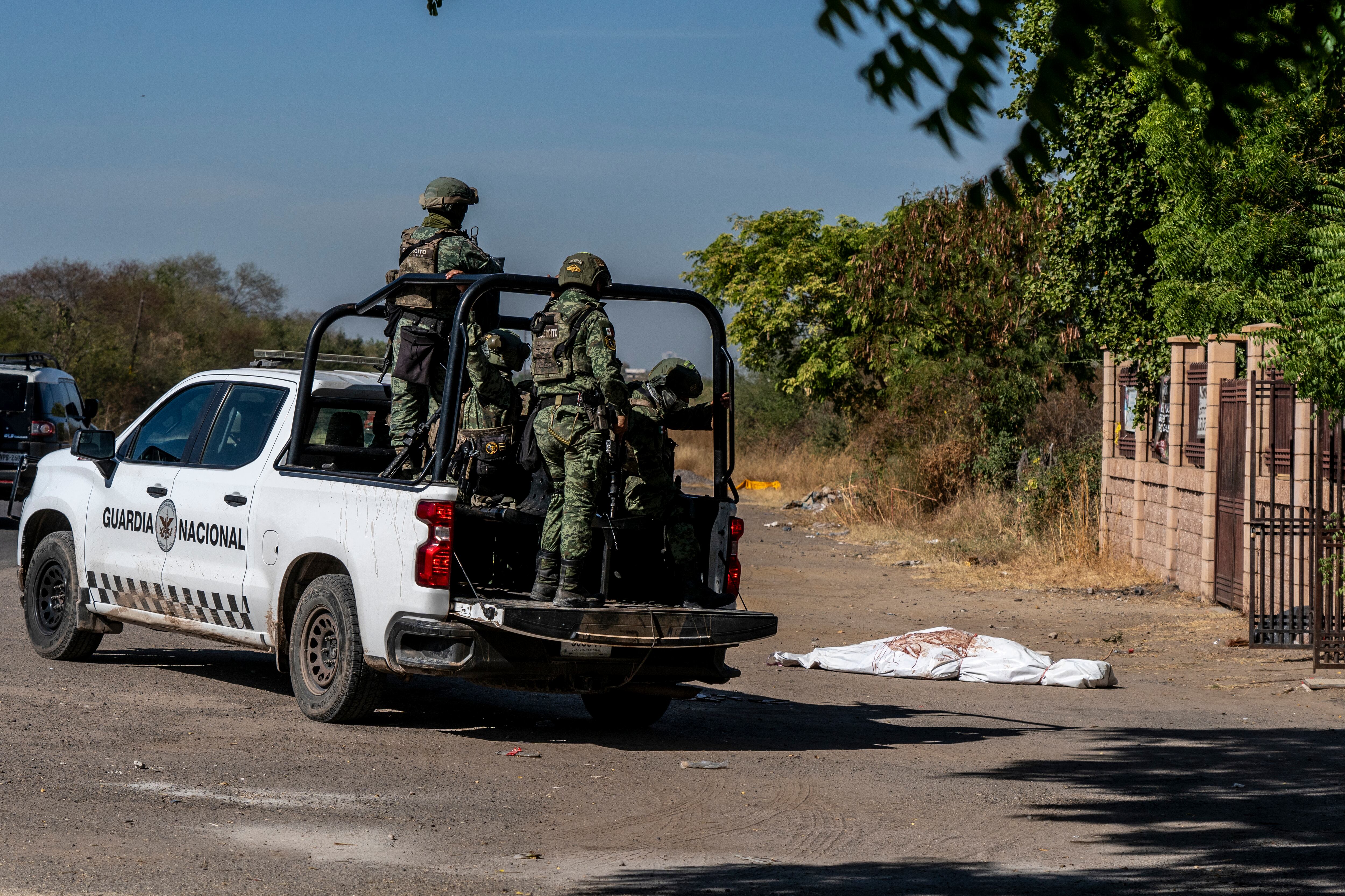 Una patrulla de la Guardia Nacional al pasar junto al cuerpo de una persona presuntamente asesinada en la entrada de un panteón en la comunidad de El Carrizalejo en Culiacán, México. el 27 de noviembre de 2024.