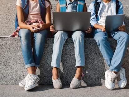 Tres jóvenes consultan dispositivos digitales en una imagen de archivo