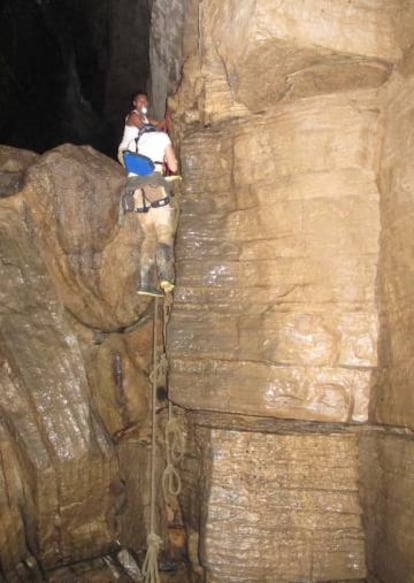 Un shuar ayuda a un visitante a escalar por una de las paredes cuadradas de la cueva.