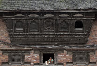 Una mujer de Nepal se asoma por la ventan de su vivienda de madera junto con su perro, en Bhaktapur.