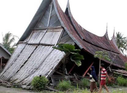 Ciudadanos indonesios caminan frente a un casa tradicional del país destruida después del terremoto que ha sacudido la isla de Sumatra.