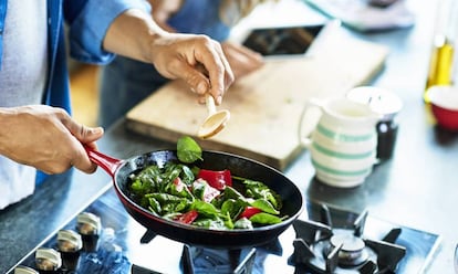 Un hombre preparada una ensalada con una sartén.