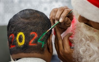 Un peluquero vestido con un traje de Santa Claus colorea los dígitos del número 2024 sobre la nuca de un hombre para dar la bienvenida al Año Nuevo, en Ahmedabad (India).