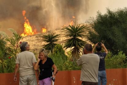 Varias personas observan cómo el incendio avanza frente a sus casas de Marbella.