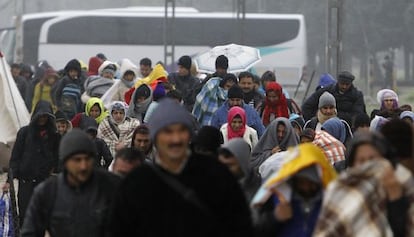 Inmigrantes y refugiados cruzan una frontera bajo la lluvia.