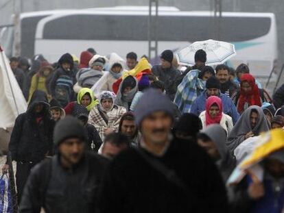 Imigrantes e refugiados cruzam fronteira sob chuva.