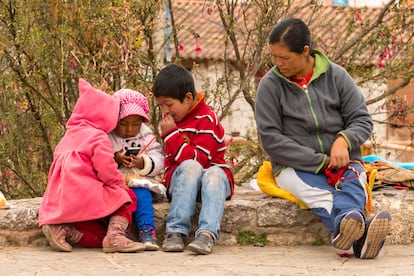 Una mujer indígena vigila a sus hijos que juegan con un teléfono móvil en Chinchero, Perú