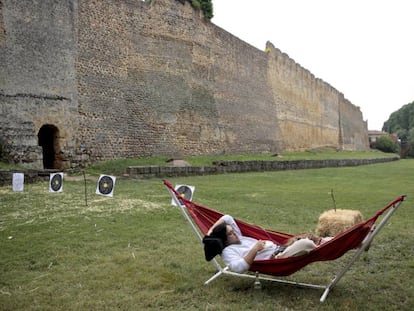 Un hombre con vestimenta medieval descansa frente a las murallas de Mansilla de las Mulas durante una celebración de feria medieval.