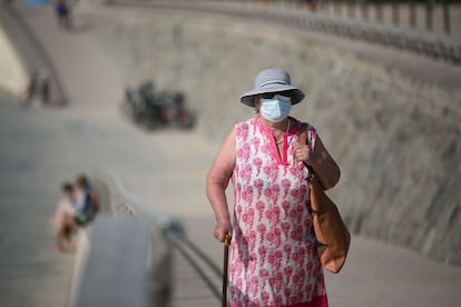 Una mujer con mascarilla camina por el paseo de la playa del Bogatell.