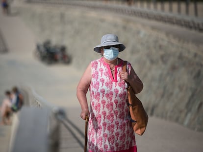 Una mujer con mascarilla camina por el paseo de la playa del Bogatell.