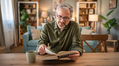 Hombre en una mesa de madera leyendo un libro junto con una taza de café.