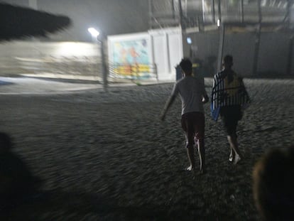 Un par de menores marroquíes que acaban de llegar a nado a la playa del Tarajal, salen caminando hacia la ciudad, en la noche de este viernes.