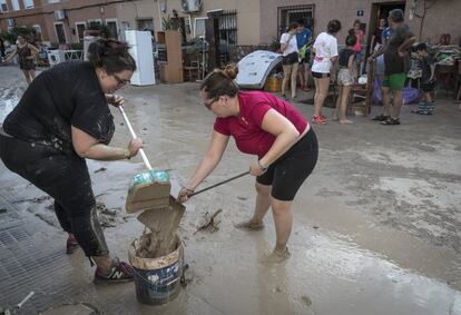 Dos vecinas de Orihuela (Alicante) tratan de retirar barro de la calle.