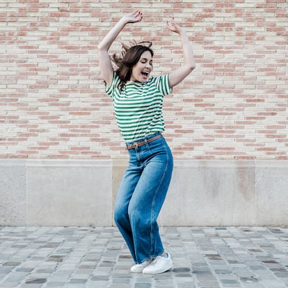 Happy middle-aged woman dancing happily, celebrating good news in front of a billet wall.