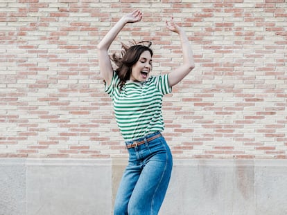 Happy middle-aged woman dancing happily, celebrating good news in front of a billet wall.