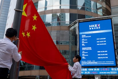 Dos personas despliegan una bandera de China frente a un monitor donde se recoge la evolución de la Bolsa de Hong Kong.