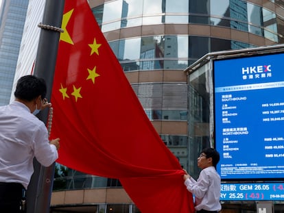 Dos personas despliegan una bandera de China frente a un monitor donde se recoge la evolución de la Bolsa de Hong Kong.