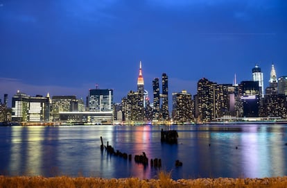El Empire State iluminado con colores se refleja en el East River, en la ciudad de Nueva York.