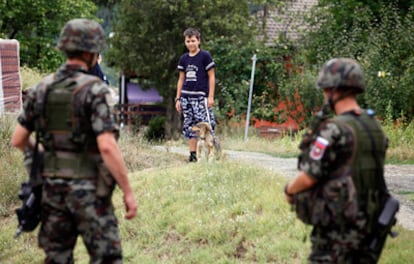 Un niño serbiokosovar observa a soldados eslovenos de la KFOR mientras pasea su perro por la localidad de Rudare.