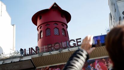 People take pictures of the landmark red windmill atop the Moulin Rouge, Paris' most famous cabaret club, after its sails fell off during the night in Paris, France, April 25, 2024. REUTERS/Benoit Tessier