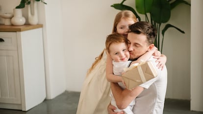 Un padre abrazando a sus dos hijos que le están dando un regalo.