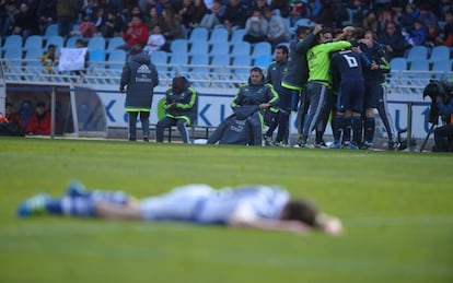 Un jugador de la Real tendido en el césped mientras los jugadores del Real Madrid celebran el gol de la victoria.