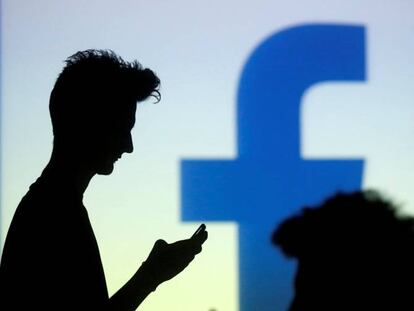 Varias personas miran sus móviles junto a un logo de Facebook.