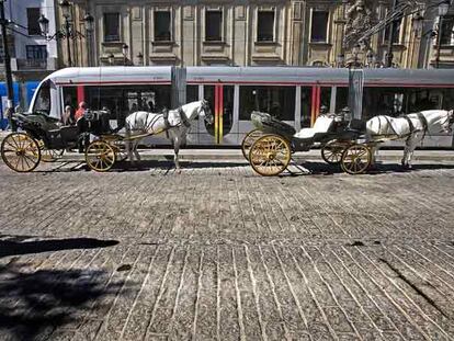 El tranvía pasa junto a los tradicionales coches de caballos por la avenida de la Constitución.