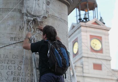 Uno de los voluntarios quita los cordeles que han servido para tender toldos y pancartas desde la estatua ecuestre de la Puerta del Sol al anochecer.