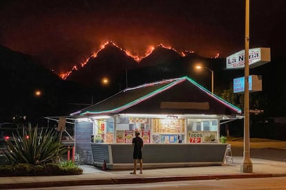 Un hombre en un restaurante de comida rápida mientras al fondo se ven las llamas que devoraban el pasado jueves por la noche las colinas del Parque Nacional de Los Ángeles.