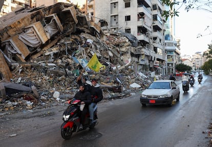 Un hombre sujeta una bandera de Hezbolá mientras pasa en moto cerca de un edificio colapsado por un bombardeo israelí en Beirut, este miércoles.  