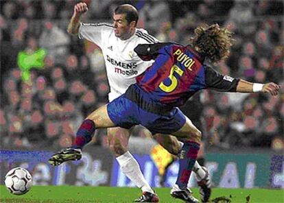 El defensa del F.C. Barcelona Carles Puyol trata de frenar el avance del centrocampista del Real Madrid Zinedine Zidane.