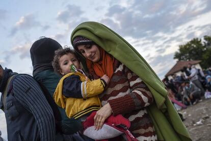 Una mujer que se ha cubierto con una manta sostiene un niño en brazos mientras espera permiso para entrar al campo de registro el lunes 19 de octubre de 2015 después de cruzar la frontera entre Grecia y Macedonia, cerca de la ciudad de Gevgelija, Macedonia.