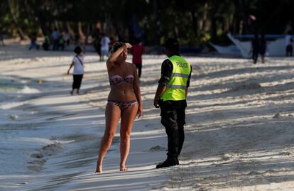 El jueves por la mañana la policía comenzó a patrullar la playa para vigilar el cumplimiento de la prohibición de nadar, a excepción de un área delimitada. En la imagen, un agente de policía habla con una turista, el 26 de abril de 2018.