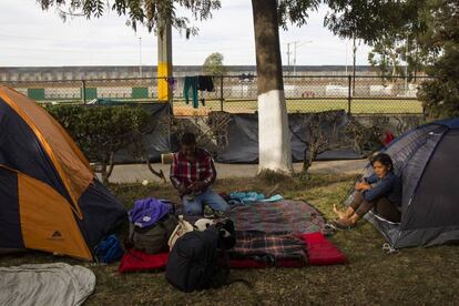 Migrantes acampan en el albergue temporal para la caravana en Tijuana. Al fondo, la valla fronteriza entre México y Estados Unidos.
