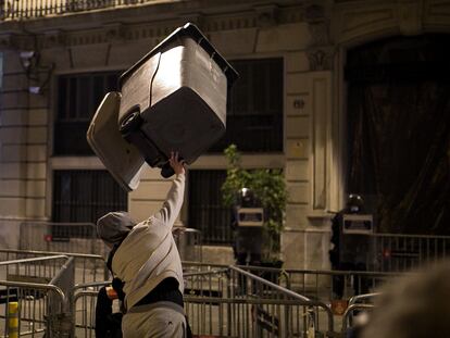 Un joven lanza un contenedor contra agentes antidisturbios de los Mossos este domingo en Barcelona.