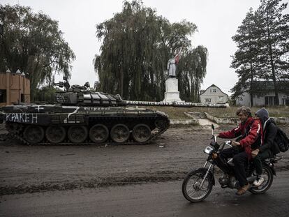Dos ucranios pasan el día 14 en moto por delante de un tanque ruso en Izium, ciudad recuperada por el ejército de Kiev.