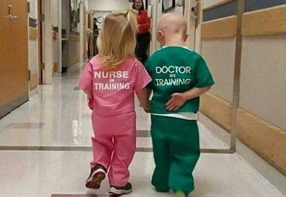 Una niña y un niño andan juntos por el pasillo de un hospital con ropa de personal médico.