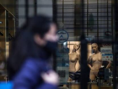 Una mujer con mascarilla pasa delante de un negocio cerrado.